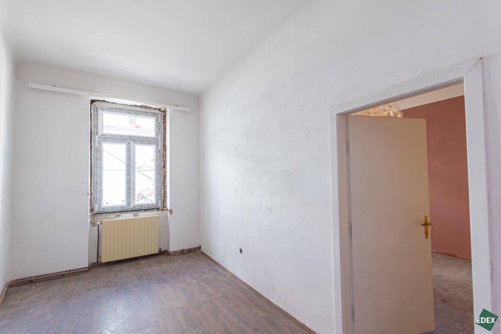 Heller, unmöblierter Raum mit weißen Wänden, einem Fenster und Heizkörper.