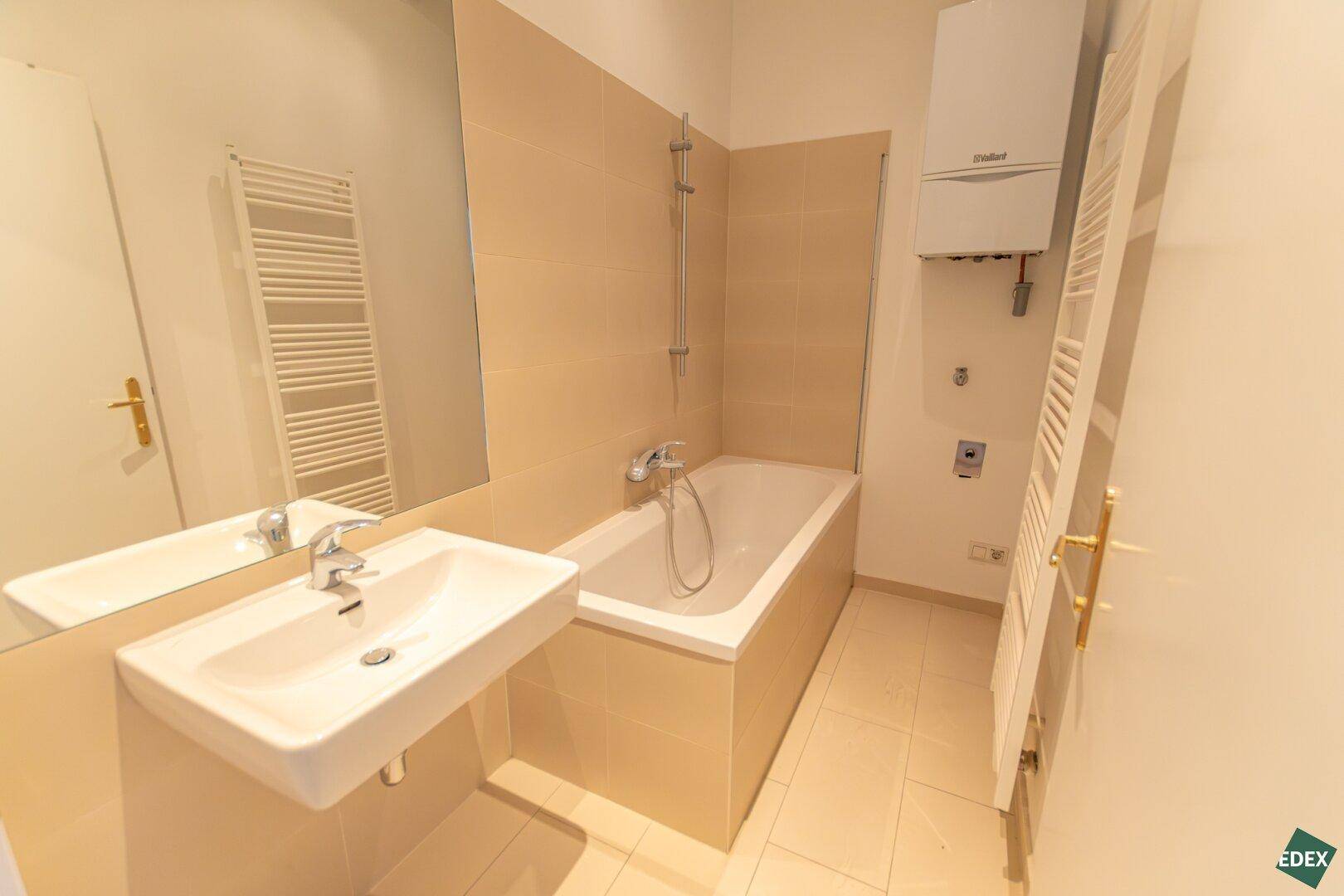 Modernes Badezimmer mit Badewanne, Waschbecken und beheiztem Handtuchhalter.