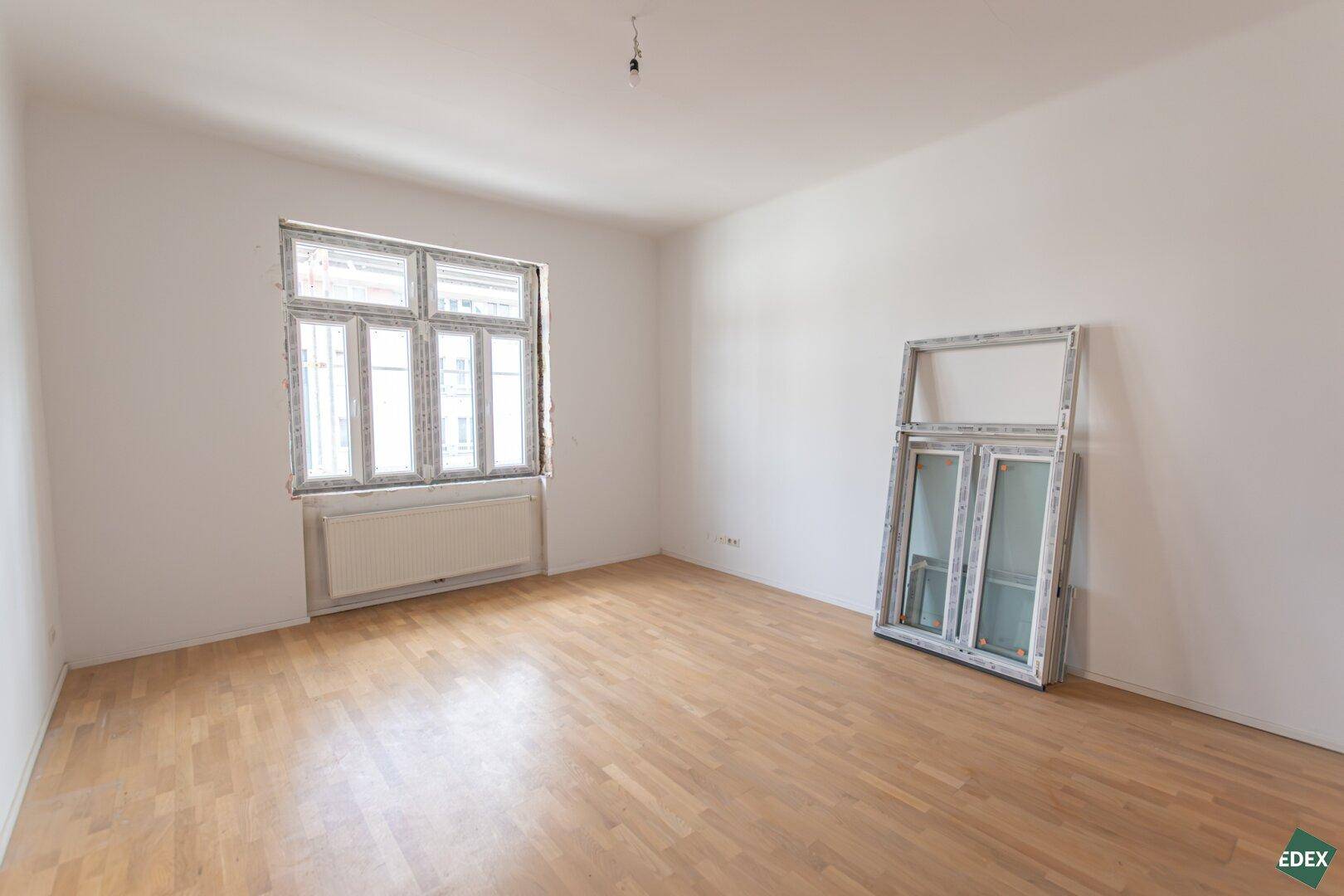 Helles Zimmer mit Parkettboden und einem großen Fenster, ein neues Fenster steht bereit.