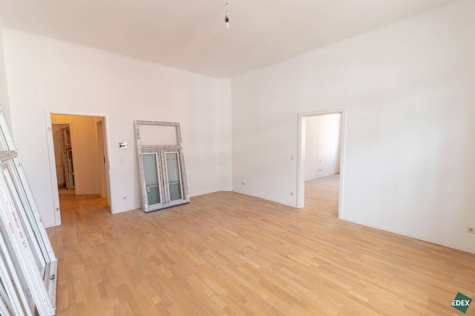 Großes, leeres Zimmer mit Parkettboden und mehreren Türöffnungen zu anderen Bereichen.