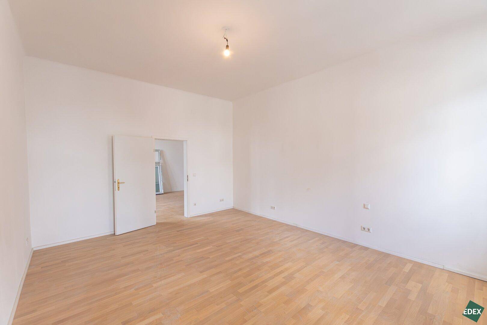 Geräumiges, leeres Zimmer mit Parkettboden und Zugang zu weiteren Räumen.