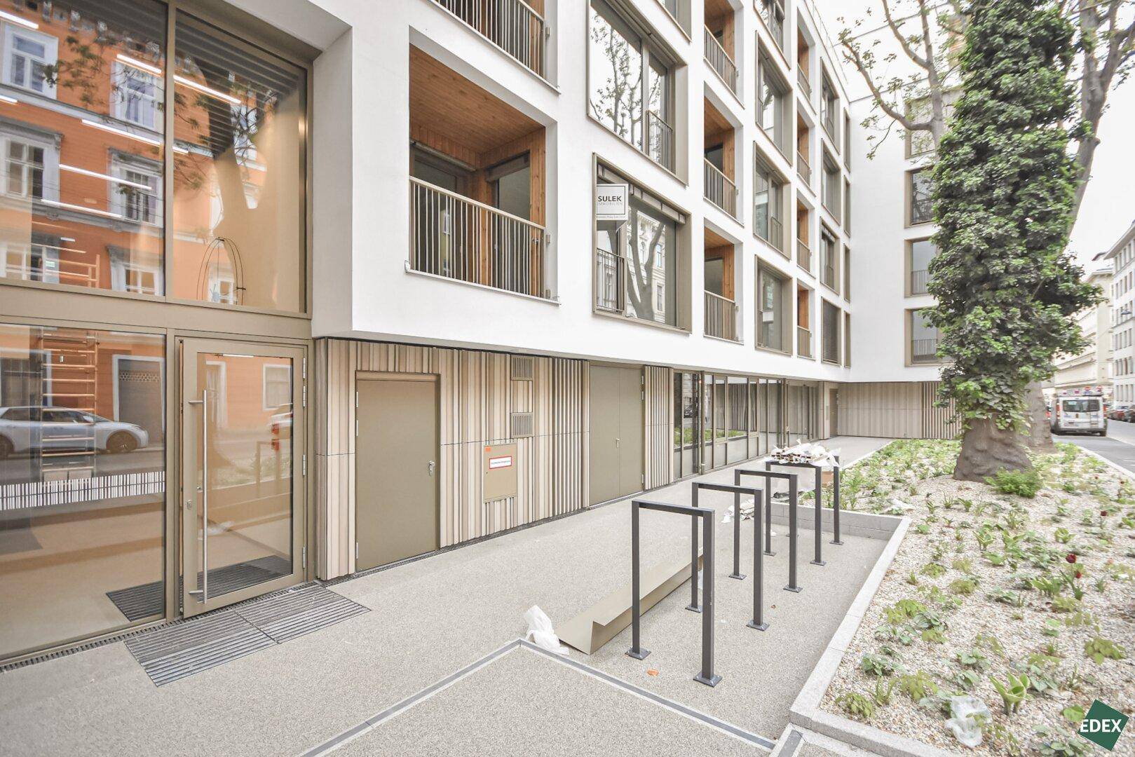 Neubau mit moderner Fassade, großen Fenstern und Fahrradständern im Eingangsbereich.