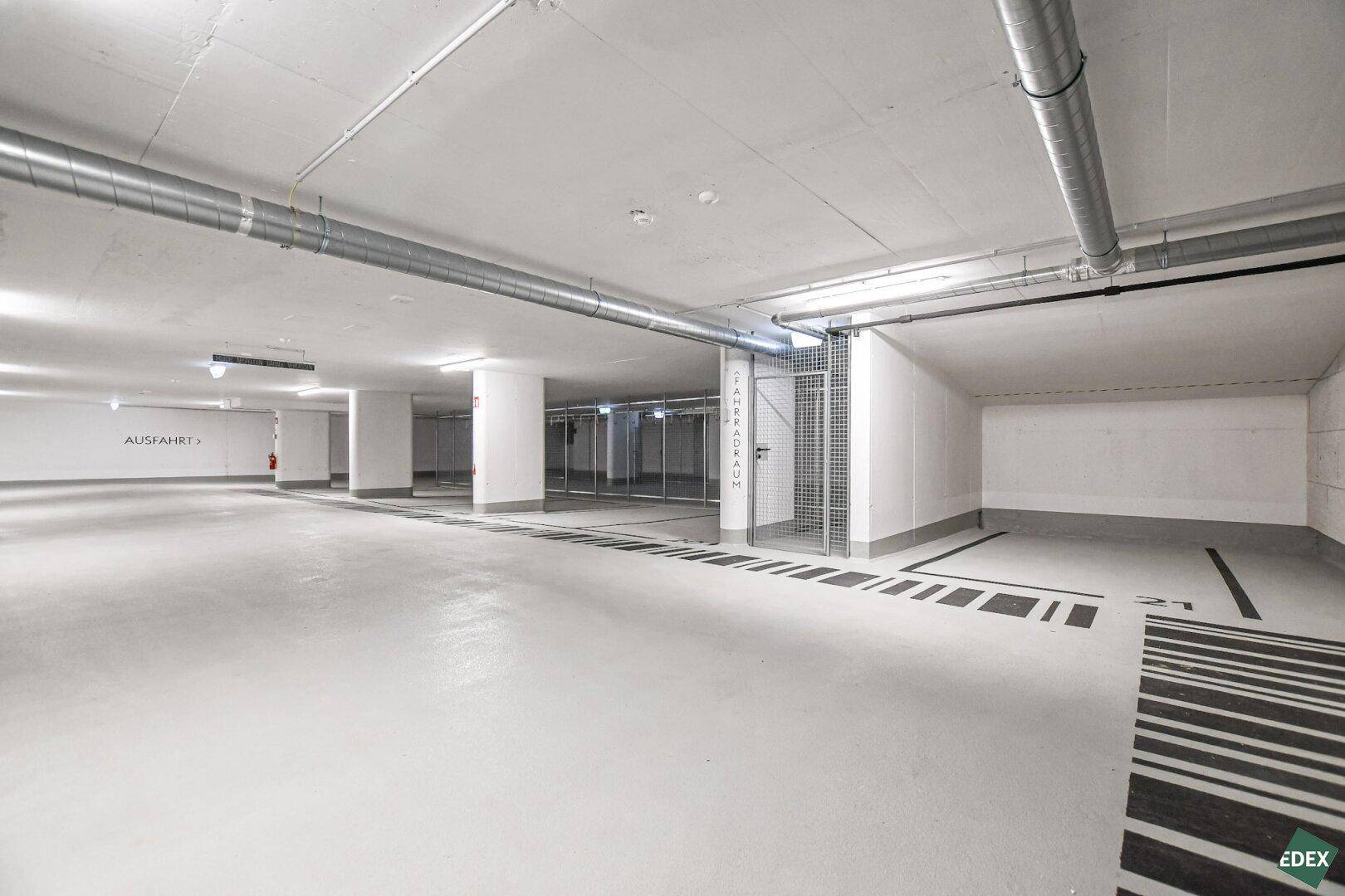 Weitläufige Tiefgarage mit klar gekennzeichneten Parkflächen und Zugang zum Fahrradraum.