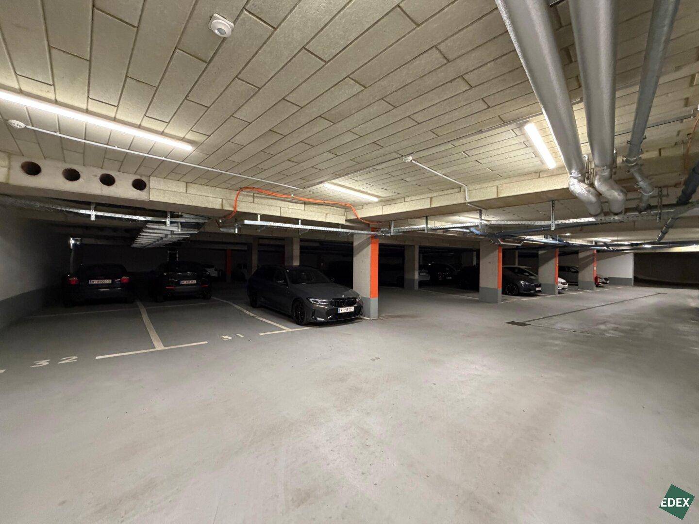 Geräumige Tiefgarage mit markierten Stellplätzen, Betonstützen und Deckenplatten, einige Fahrzeuge parken.