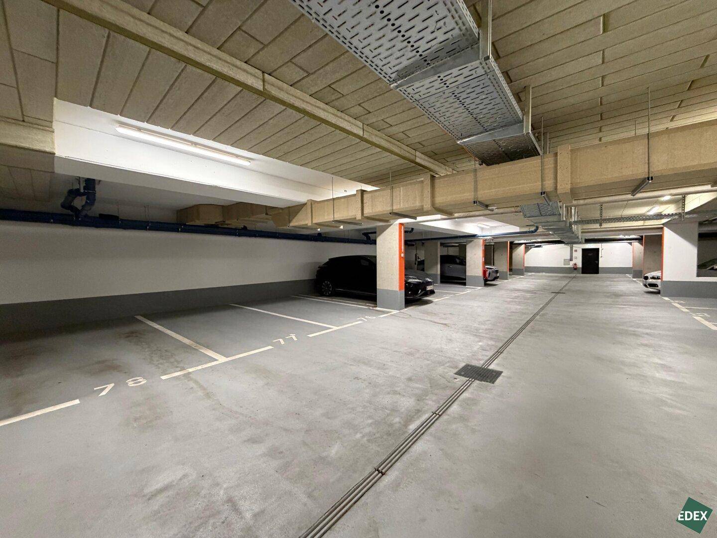 Moderne Tiefgarage mit vielen freien Stellplätzen, klaren Markierungen und technischer Infrastruktur an der Decke.