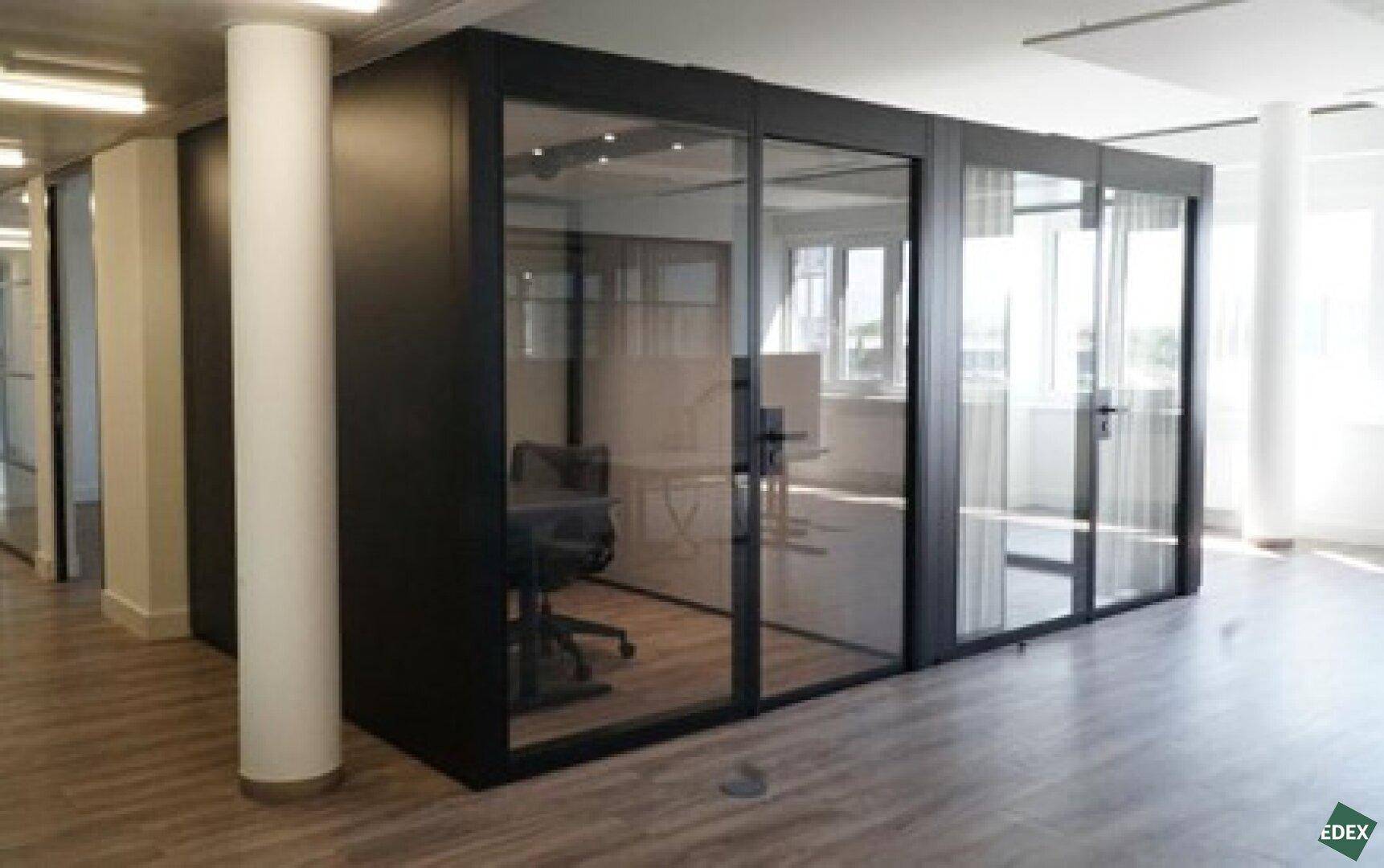 Modernes Büro mit einem gläsernen Besprechungsraum oder Einzelbüro und Holzboden.