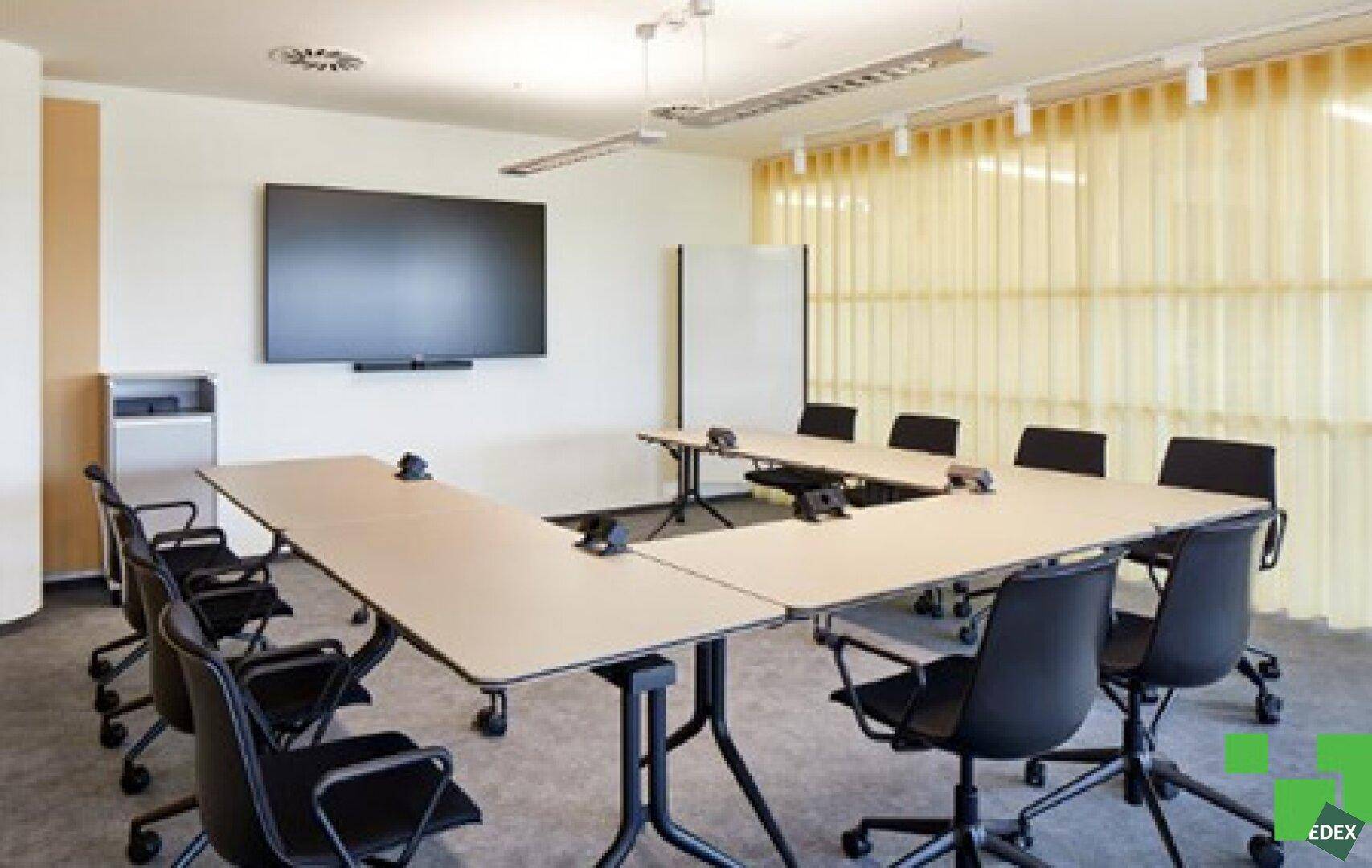 Moderner Konferenzraum mit U-förmigem Tisch, großem Bildschirm und Klimaanlage.