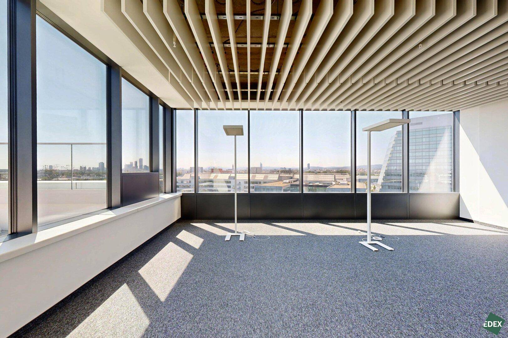 Helles Eckbüro mit großen Fenstern, Lamellendecke und weitem Blick über die Stadt.