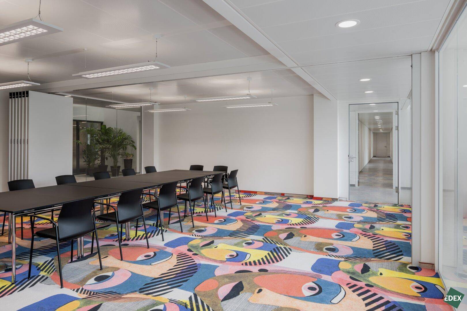 Großer Konferenzraum mit farbenfrohem Teppichboden und langer Tafel für Besprechungen.