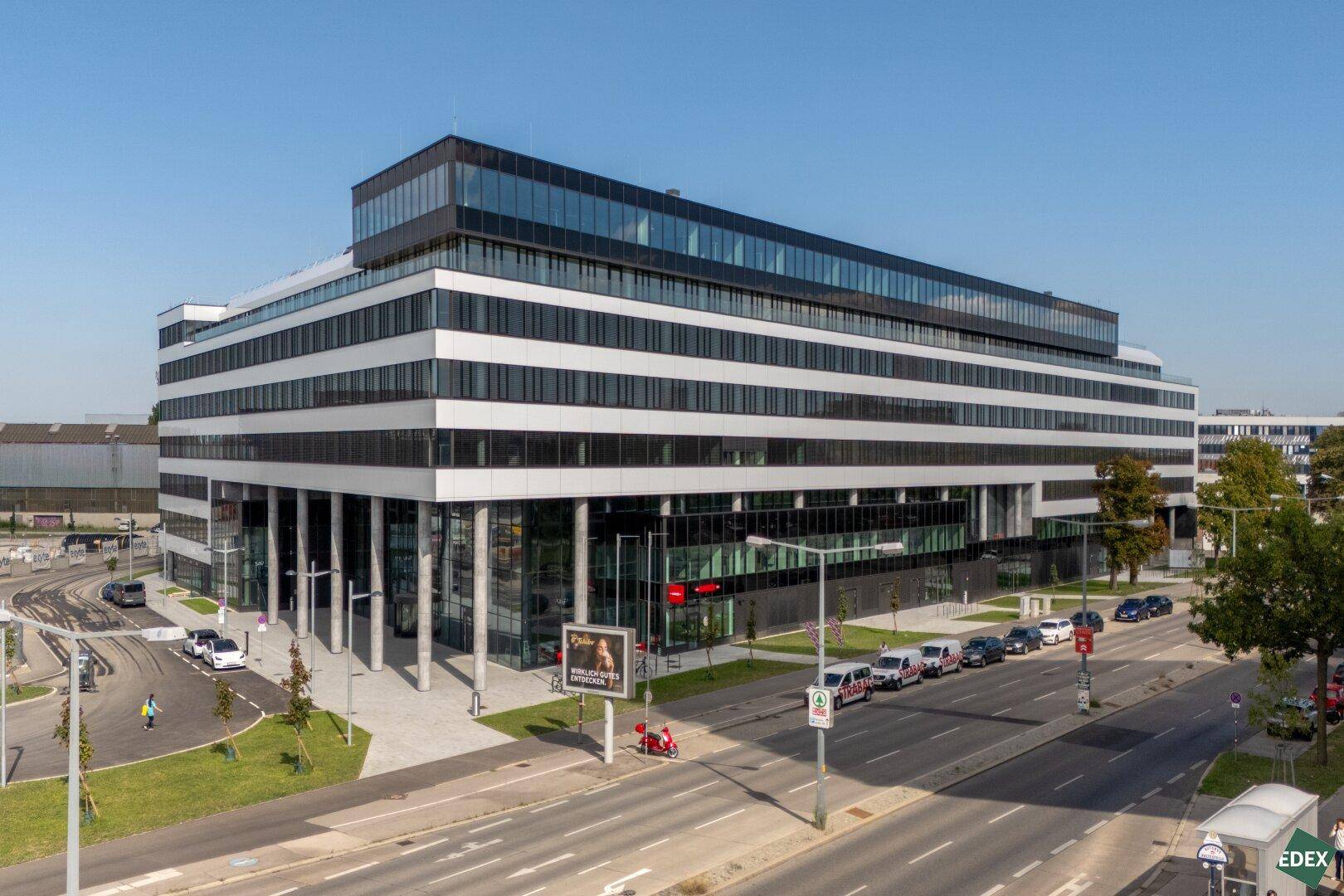 Luftaufnahme eines großen, modernen Bürokomplexes mit Glasfassade und umliegender Infrastruktur.