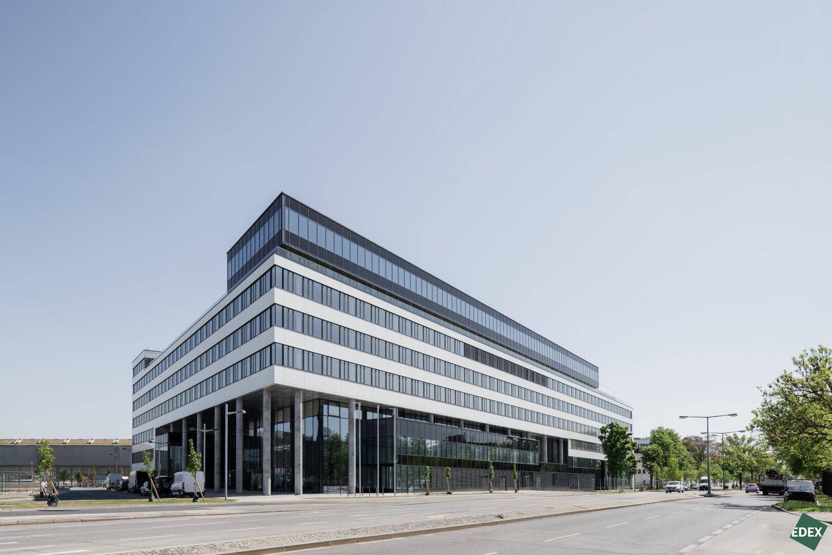 Modernes Bürogebäude mit markanter weißer Fassade, horizontalen Fensterbändern und dunklem Glasdachgeschoss.