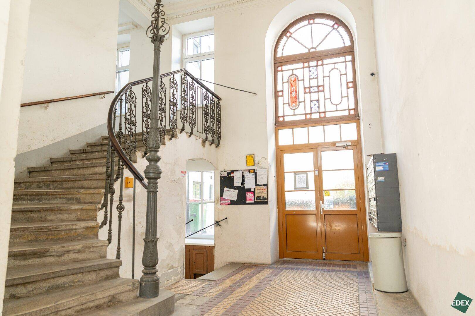 Historisches Treppenhaus mit schmiedeeisernem Geländer und einem großen Bogenfenster.