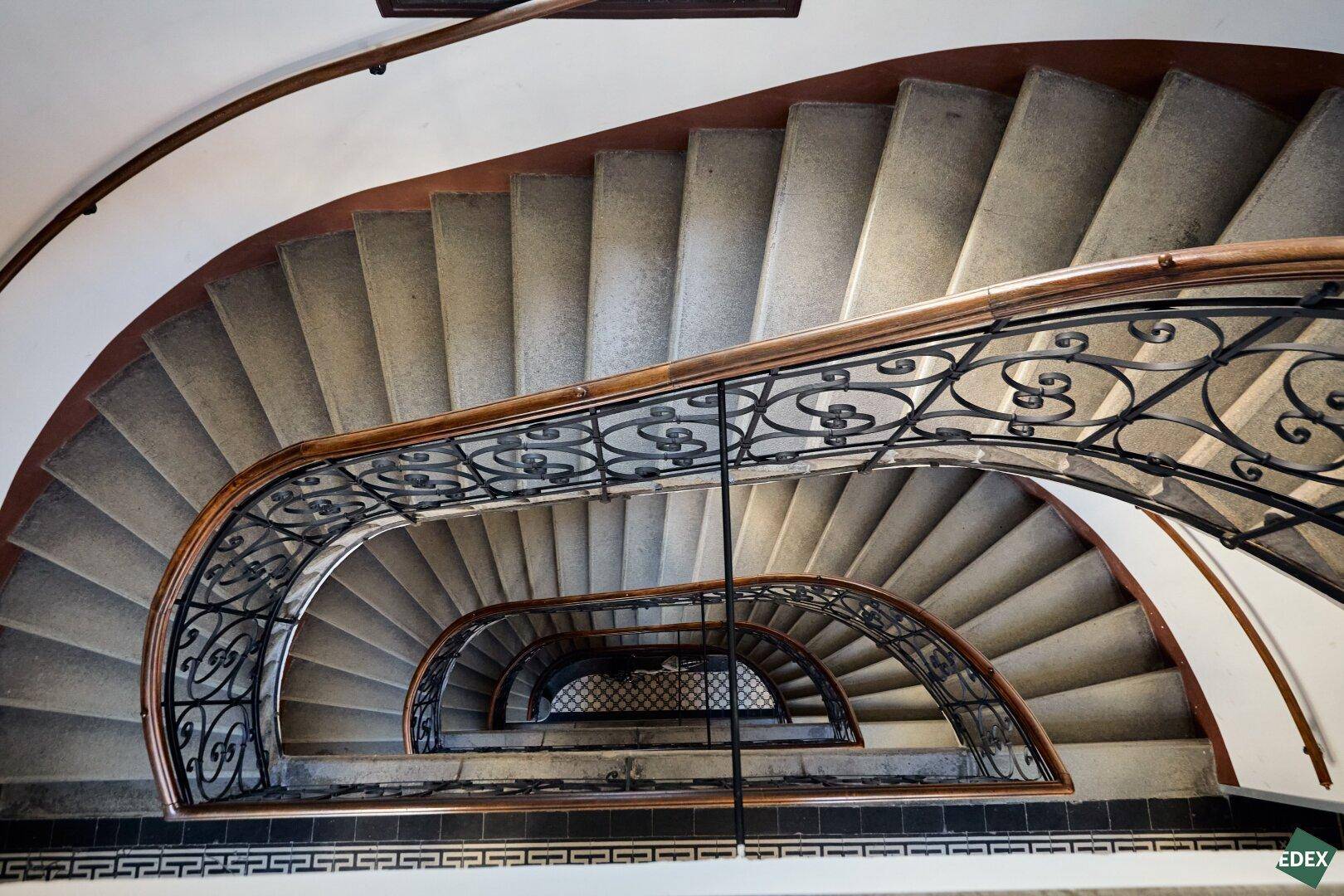 Blick von oben in ein elegantes, geschwungenes Treppenhaus mit kunstvollem Geländer.
