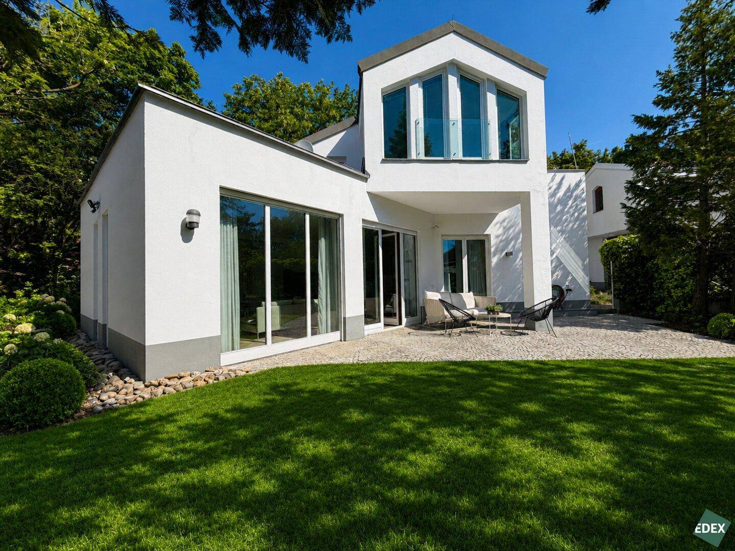 Helle Hausfassade mit großen Fensterfronten und einer einladenden Terrasse zum Garten.