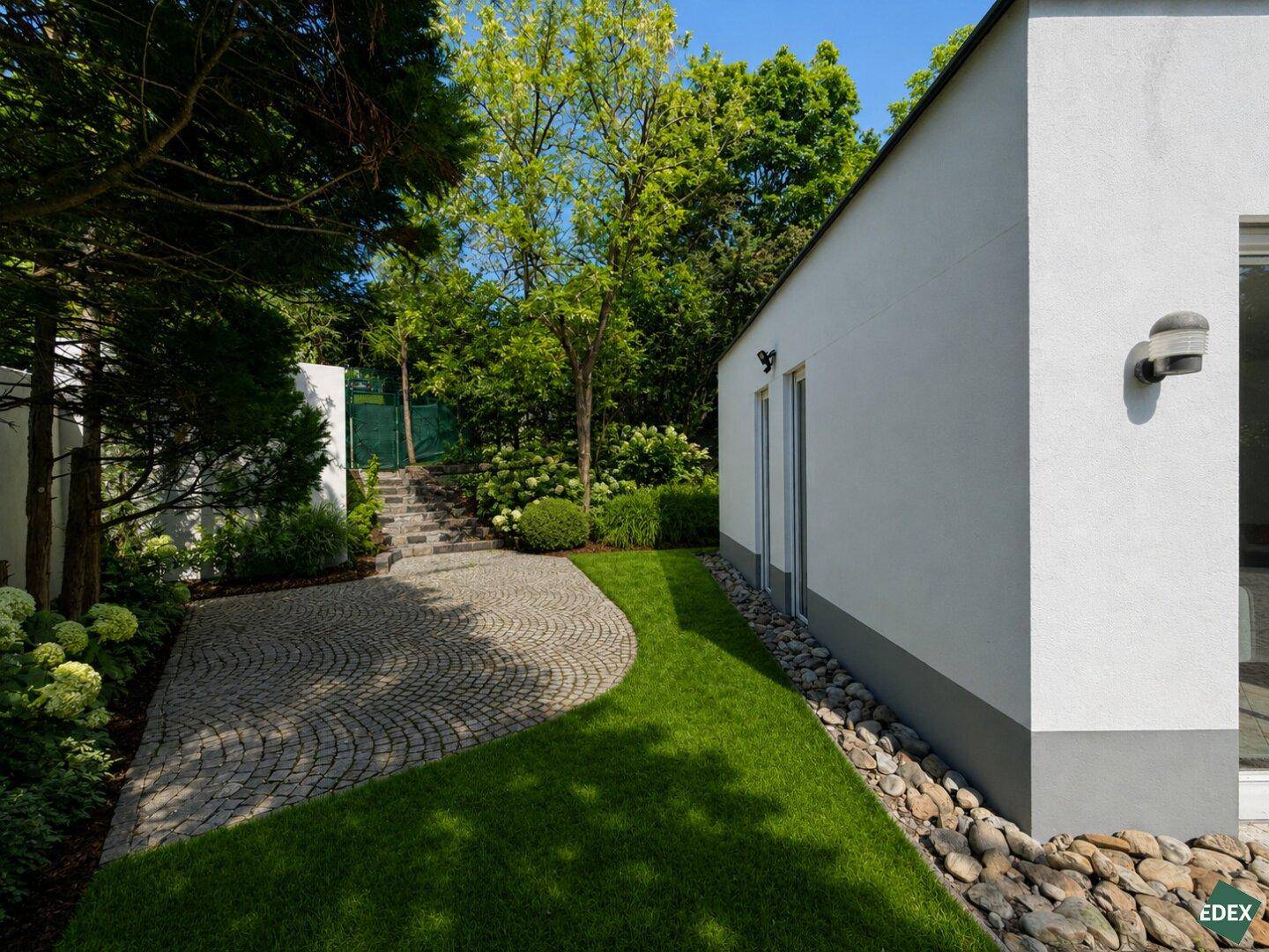 Seitlicher Gartenbereich mit geschwungenem Pflasterweg und üppiger Bepflanzung.