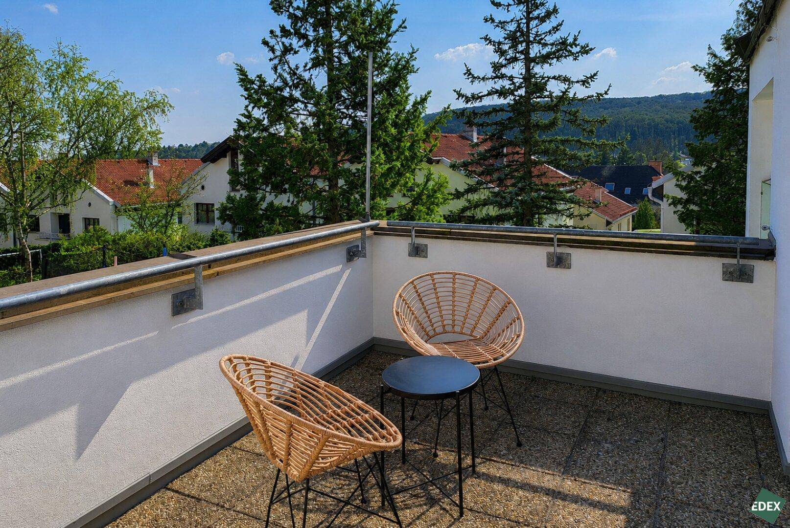 Sonniger Balkon mit Rattanmöbeln und weitem Blick über die Umgebung.