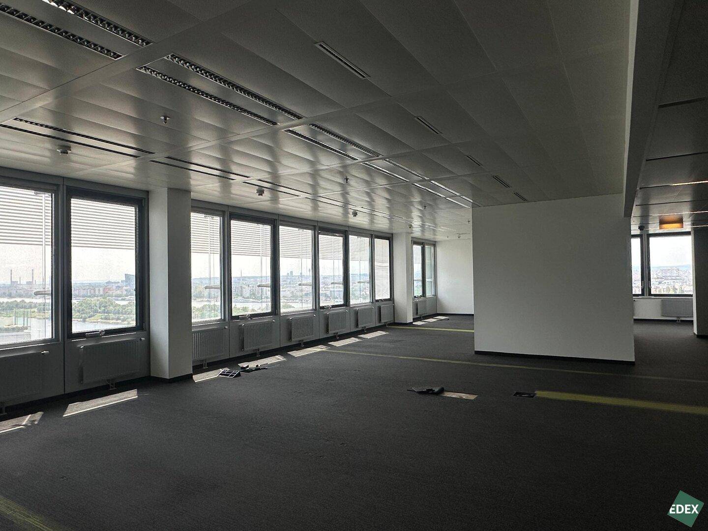 Weitläufiges, leeres Büro mit Teppichboden und Panoramablick auf die Stadt und das Wasser.