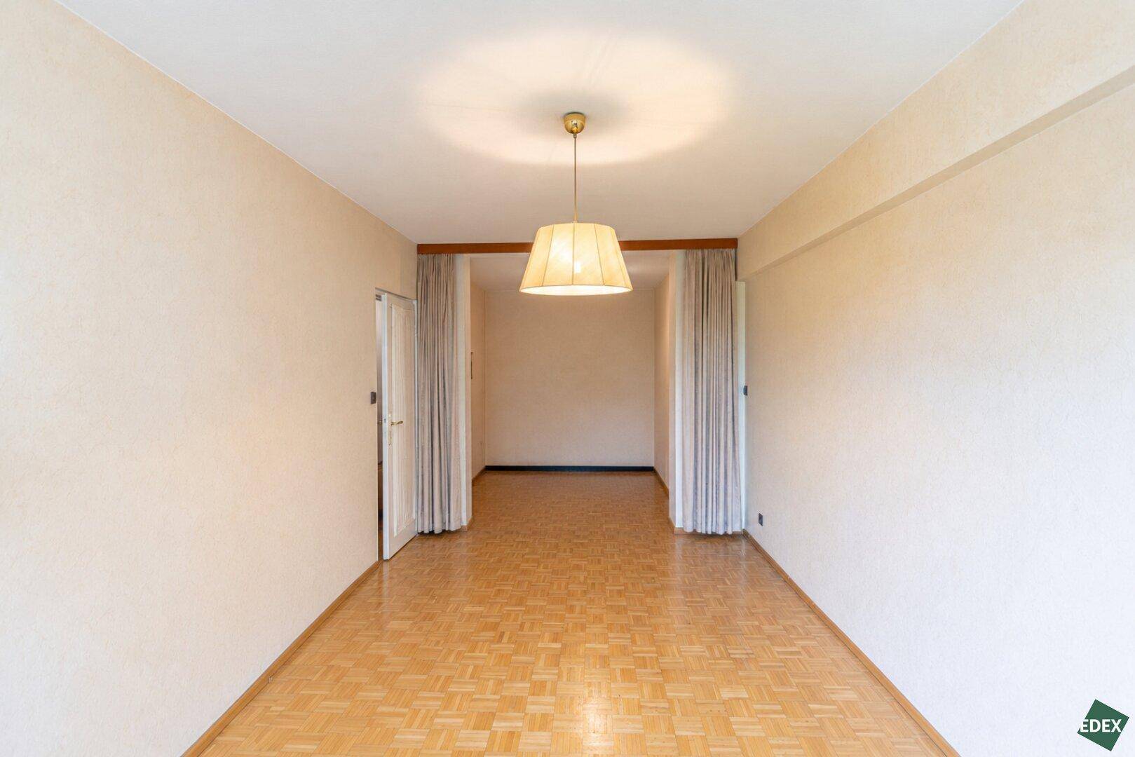 Leeres Schlafzimmer mit Parkettboden und Vorhängen, die den Eingangsbereich abgrenzen.