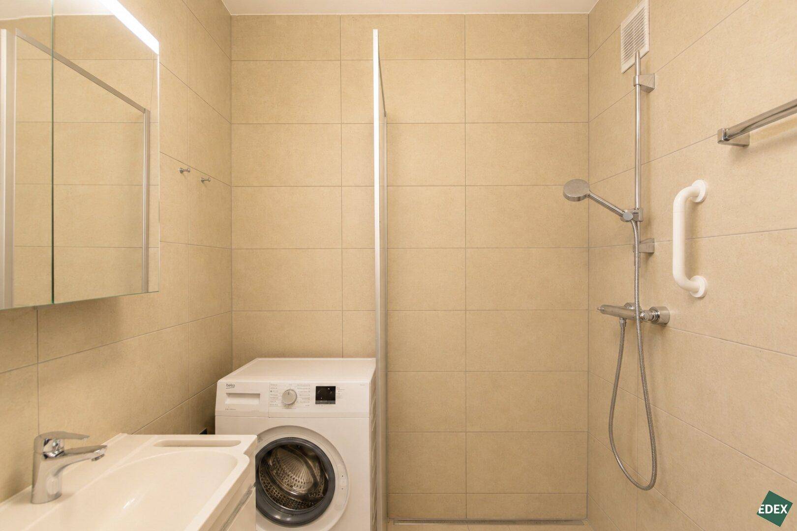 Modernes Badezimmer mit beigefarbenen Fliesen, Dusche und Waschmaschine.