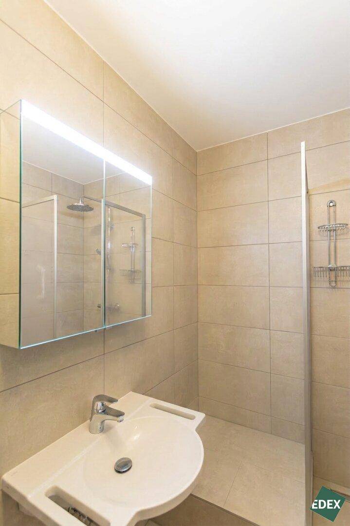 Helles Badezimmer mit beigefarbenen Fliesen, Dusche und modernem Waschbecken.