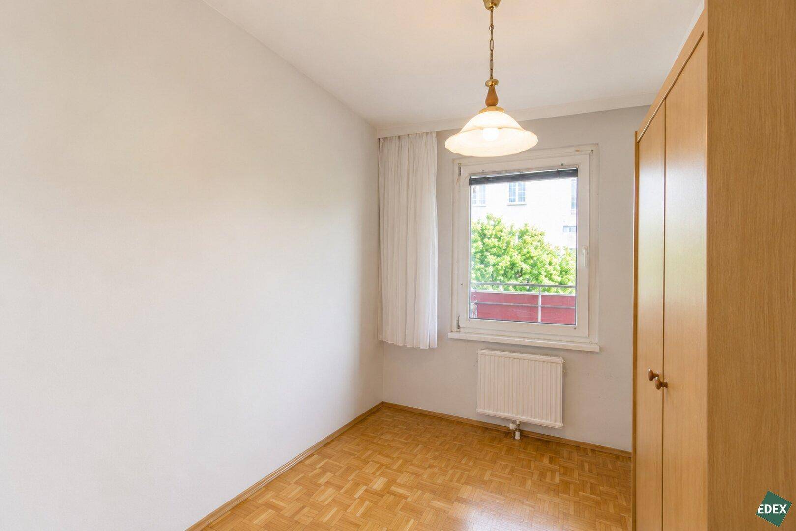 Kleines Schlafzimmer mit Parkettboden, Fenster und einem Kleiderschrank.