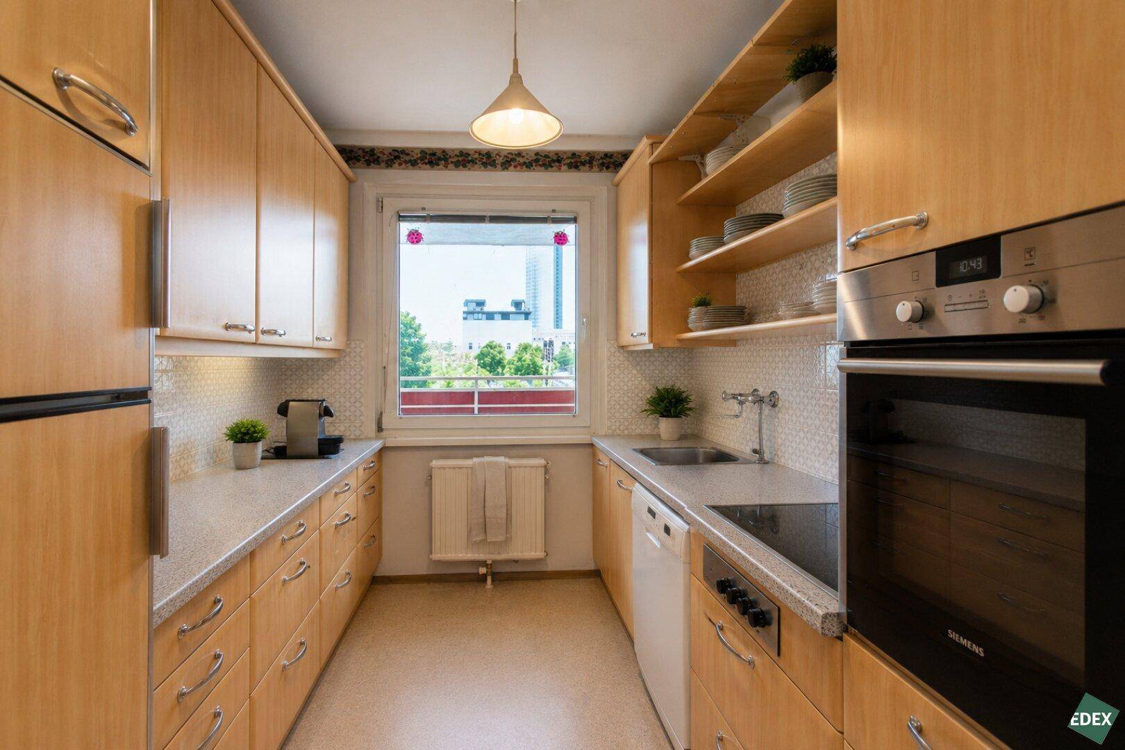 Funktionale Küche mit Holzschränken, Einbaugeräten und Fenster mit Ausblick.