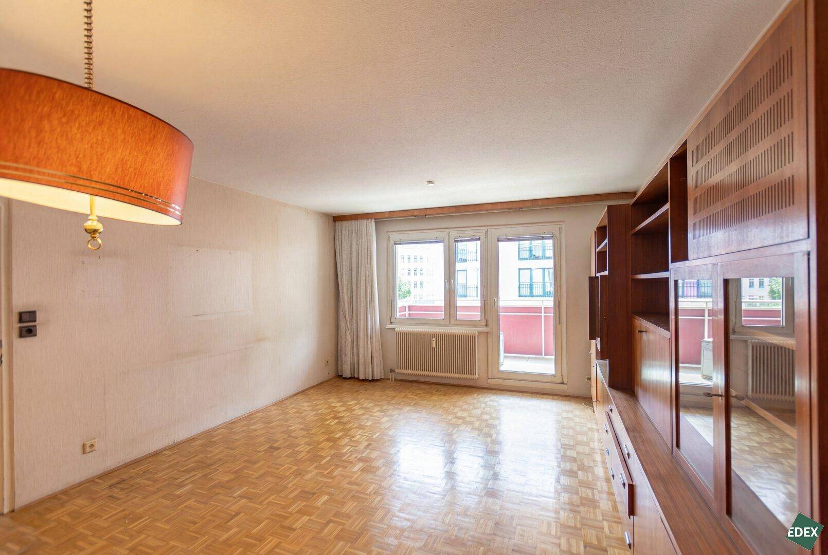 Geräumiges Wohnzimmer mit Parkettboden, Einbauschrank und Balkonzugang.