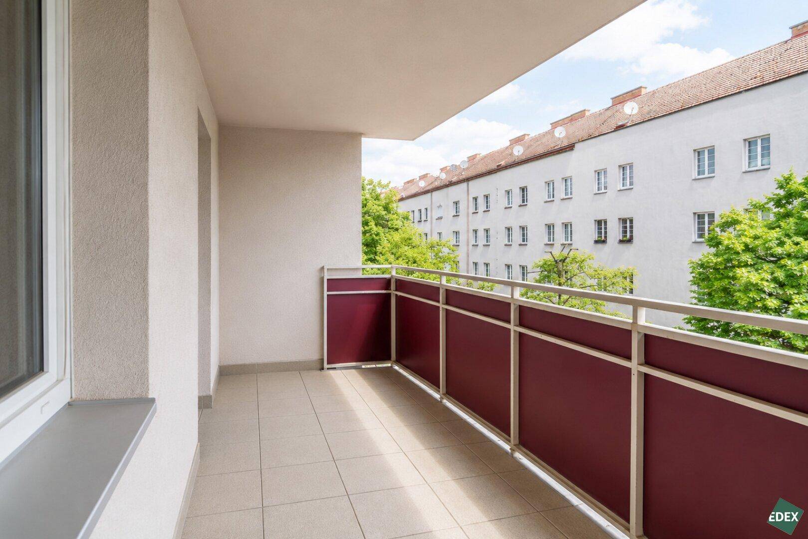 Heller Balkon mit Fliesenboden und Blick auf die umliegenden Wohngebäude.