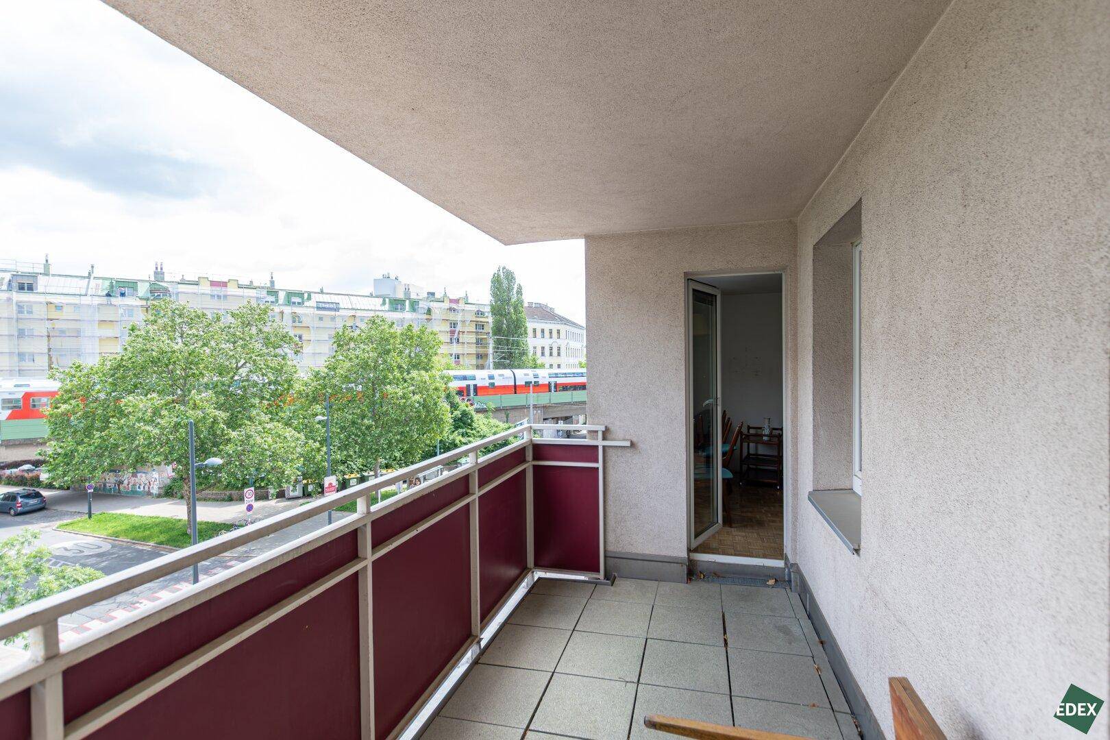 Balkon mit Blick auf die Stadt, Bäume und eine vorbeifahrende Bahn.