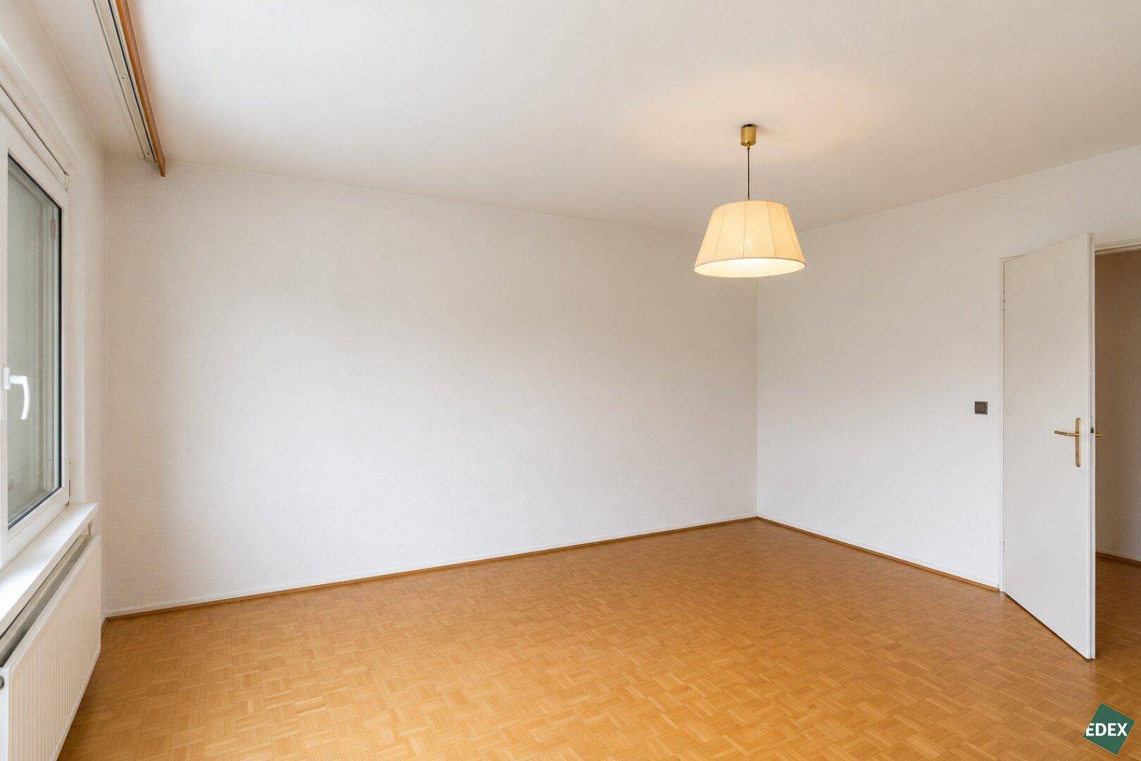 Leeres Zimmer mit Parkettboden und weiß gestrichenen Wänden, bereit zur individuellen Gestaltung.