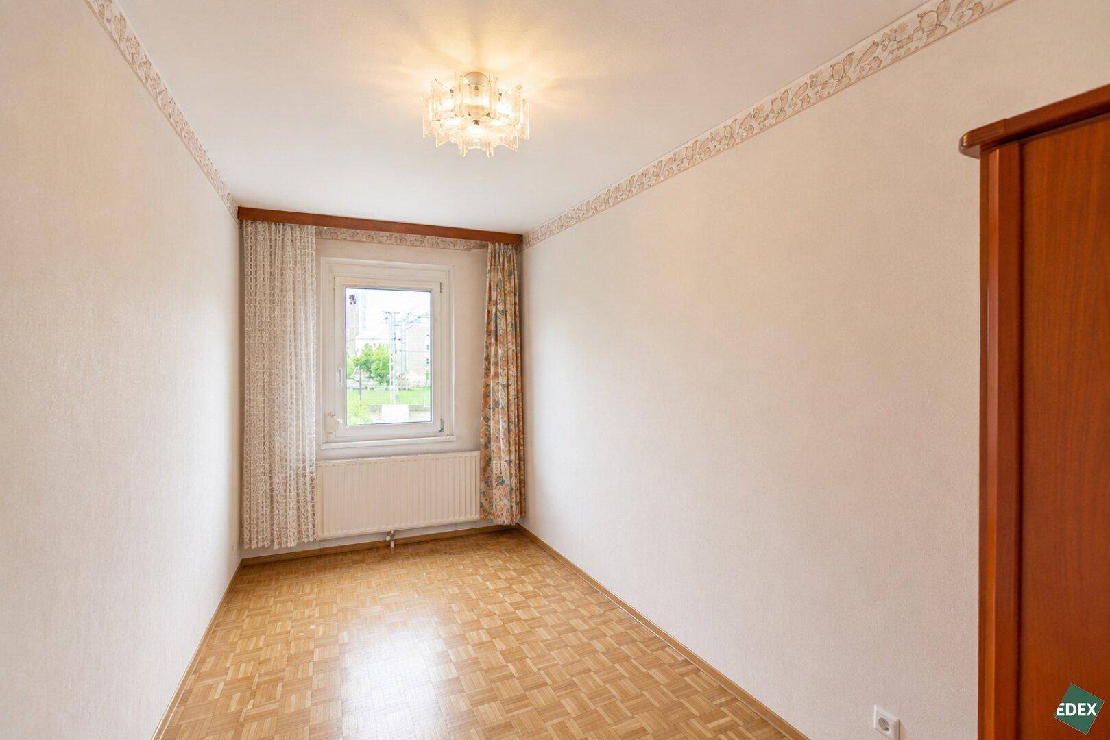Schlafzimmer mit Parkettboden, Fenster und dekorativer Tapetenbordüre.