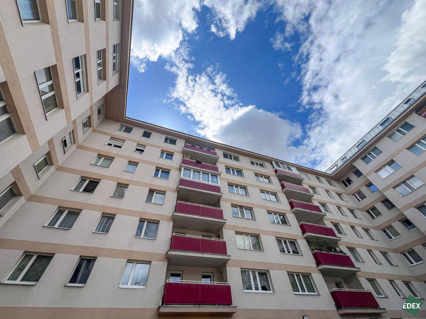 Fassade eines Mehrfamilienhauses mit zahlreichen Balkonen unter blauem Himmel.