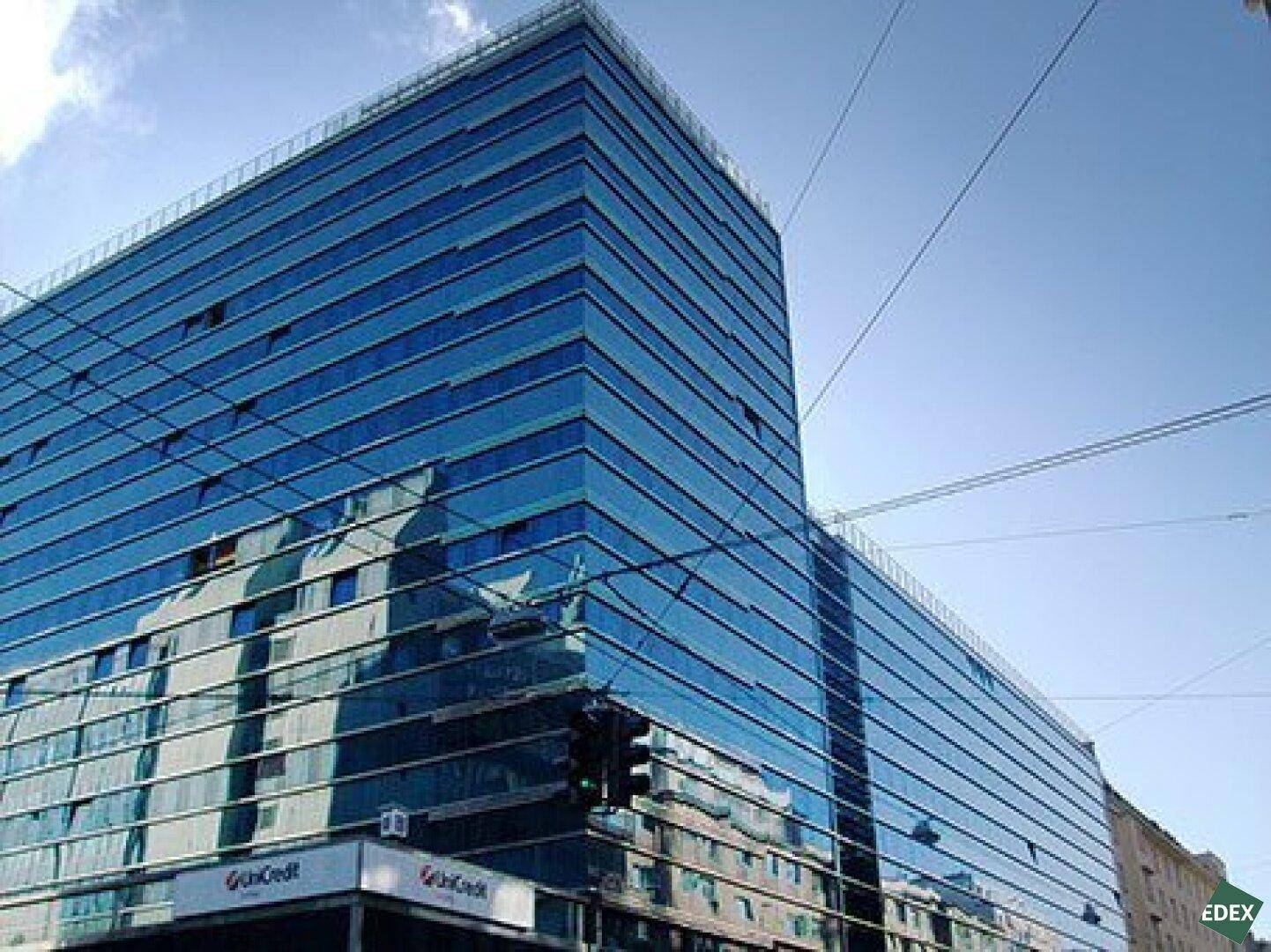 Eindrucksvolle Ecke eines modernen Bürogebäudes mit spiegelnder Glasfassade unter blauem Himmel.