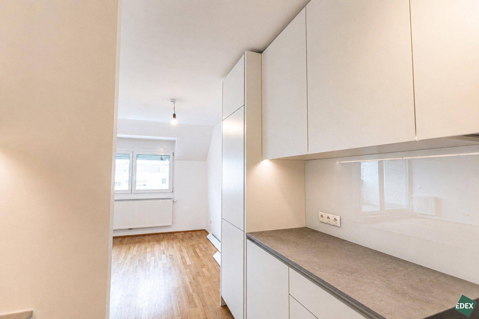 Blick vom Küchenbereich in den hellen Wohnraum mit Fenster und Heizkörper.