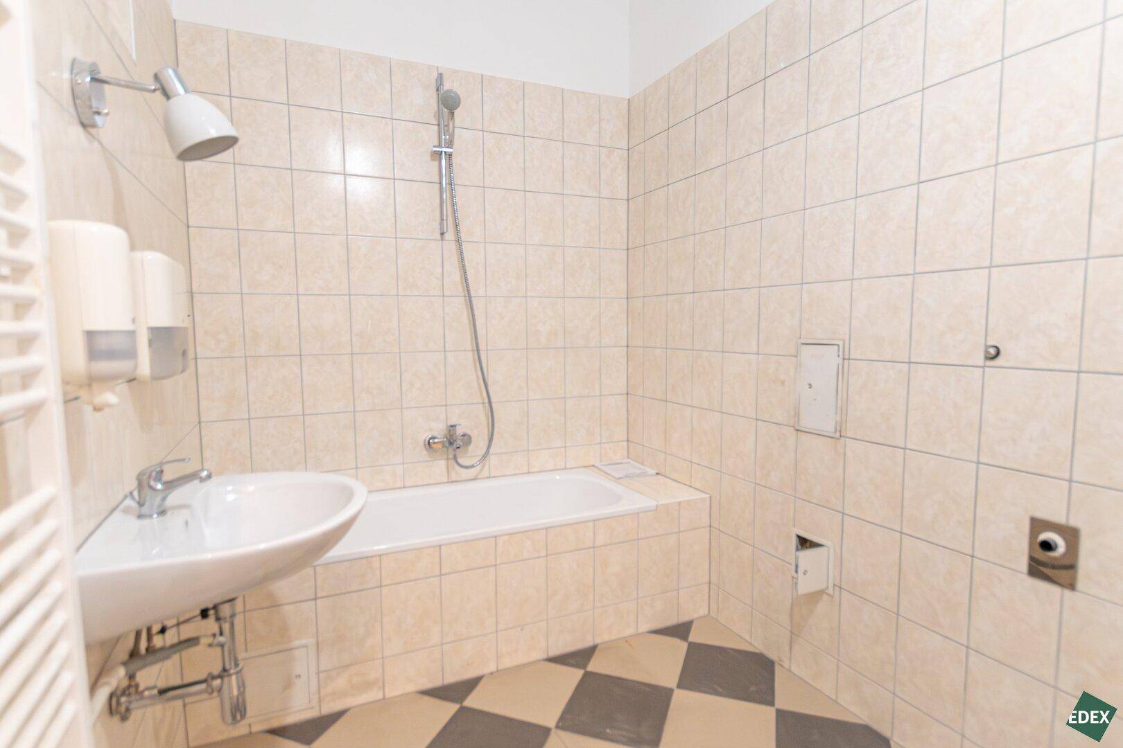 Gefliestes Badezimmer mit Badewanne, Waschbecken und Heizkörper, in hellem Beige gehalten.