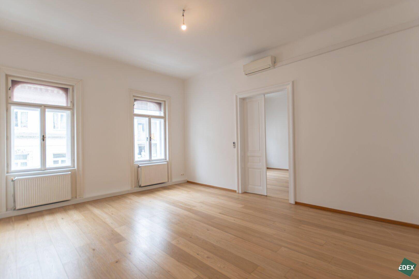 Geräumiges, helles Zimmer mit Holzboden und hohen Decken, ideal für Wohn- oder Schlafbereich.