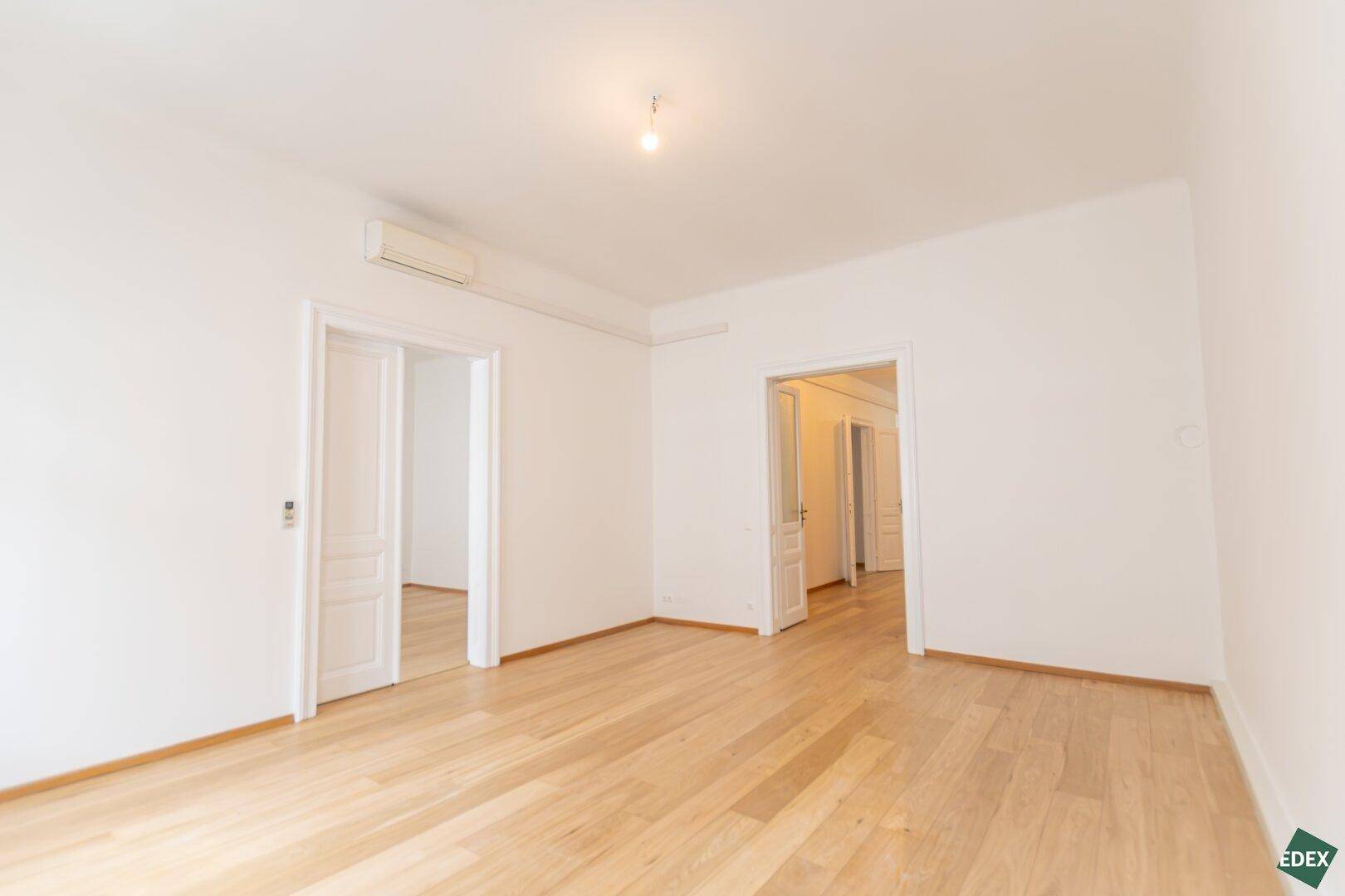 Großes, helles Zimmer mit Parkettboden und mehreren Türen, bietet flexible Raumgestaltungsmöglichkeiten.