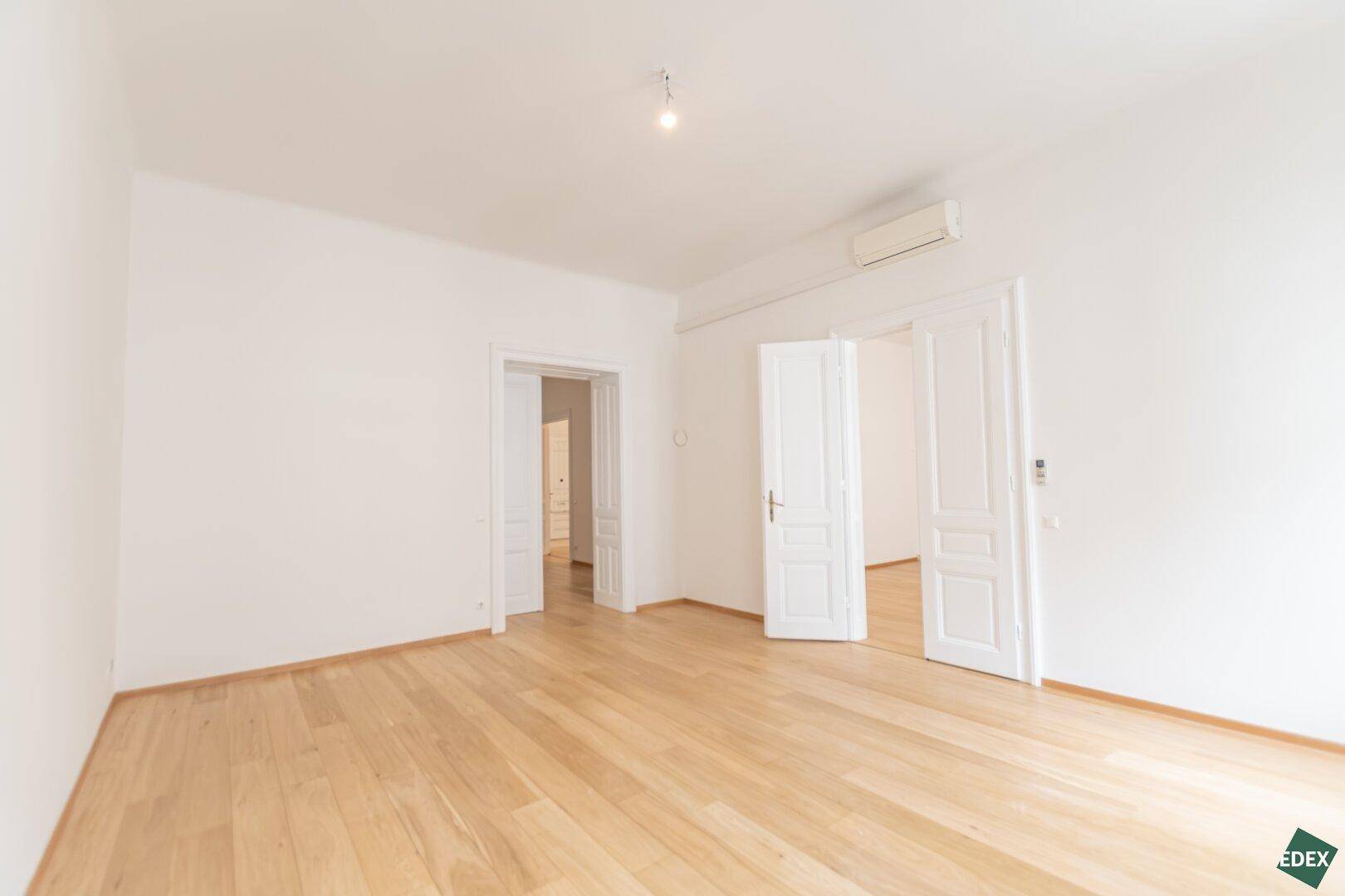 Helles Zimmer mit Parkettboden und doppelten Flügeltüren, ideal für ein großzügiges Wohnambiente.