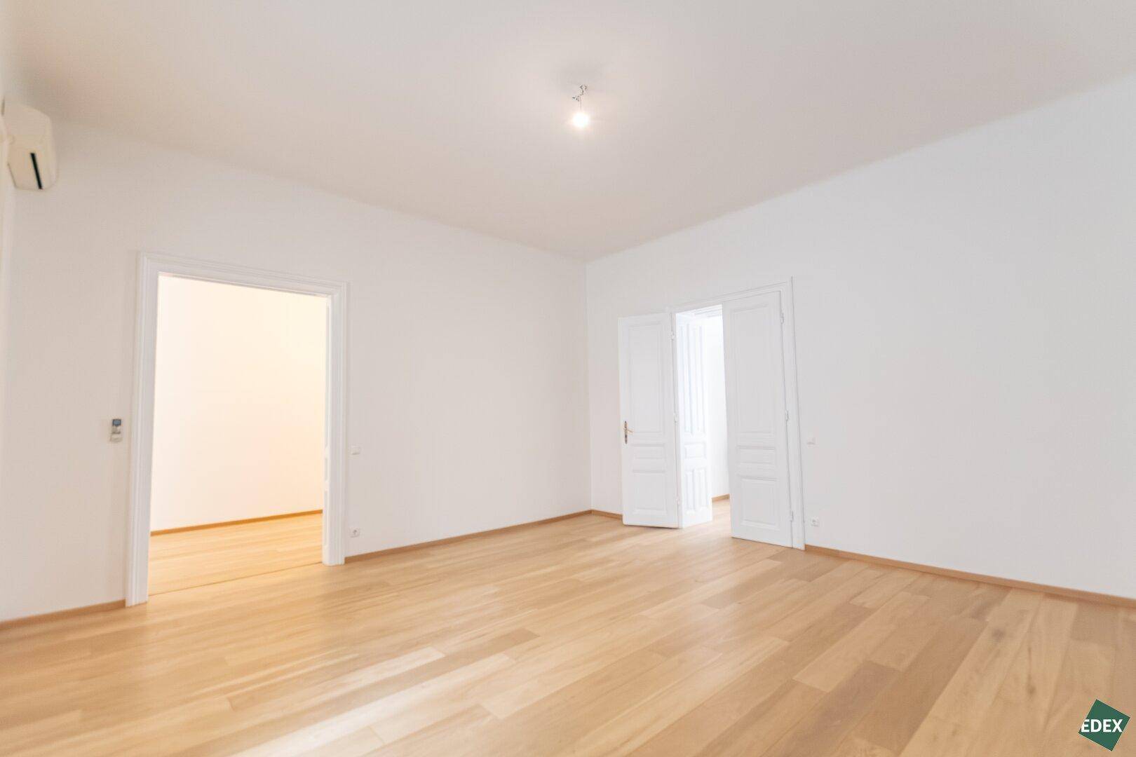 Weitläufiges Zimmer mit Parkettboden und hohen Türen, bietet viel Platz und Helligkeit.