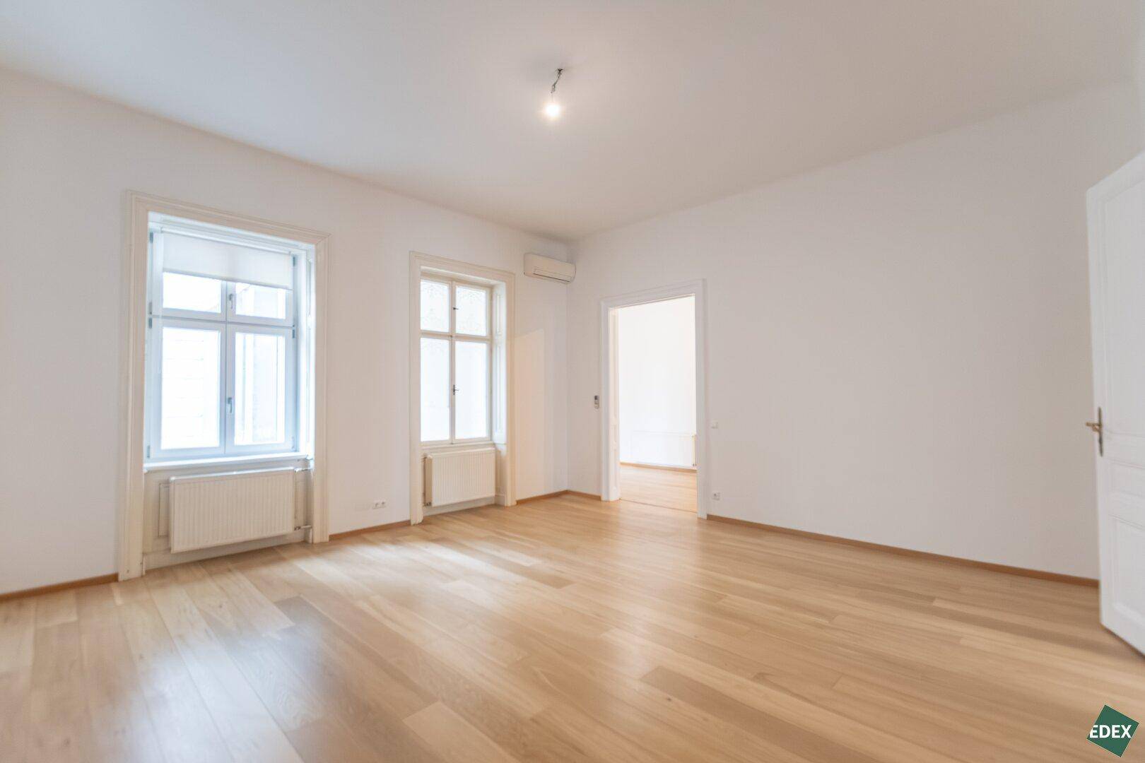 Lichtdurchflutetes Zimmer mit Parkettboden und klassischen Fenstern, bereit für neue Bewohner.