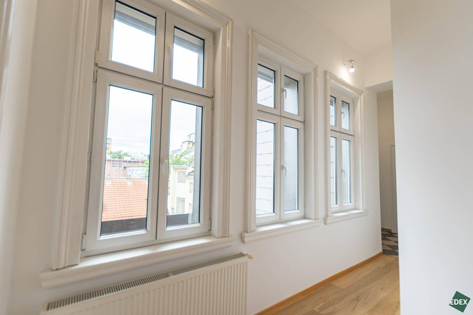 Heller Flur mit Parkettboden und einer Reihe von Fenstern, die viel Tageslicht hereinlassen.