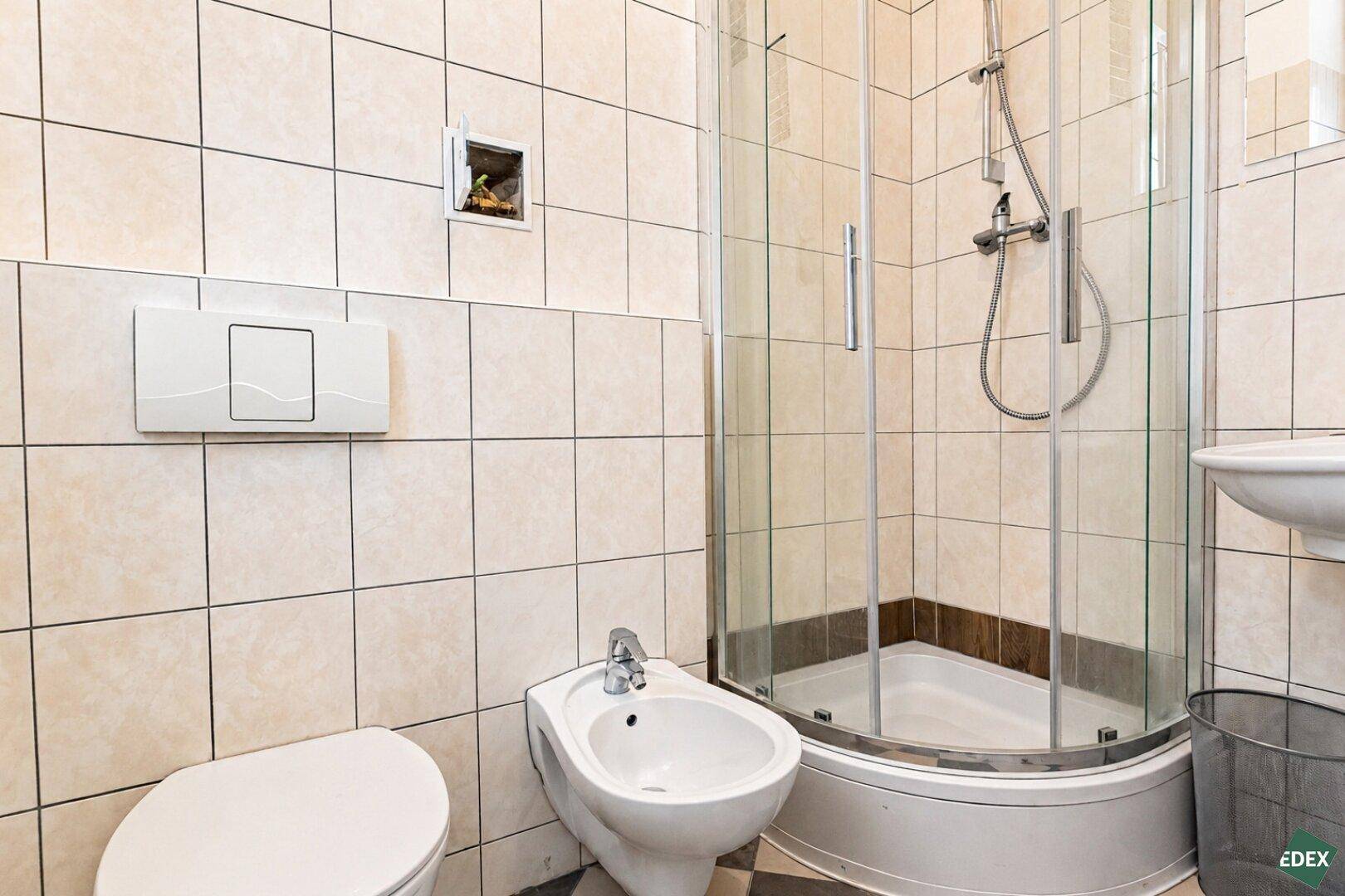 Gefliestes Badezimmer mit Duschkabine, Bidet und Toilette, in hellen Beigetönen.