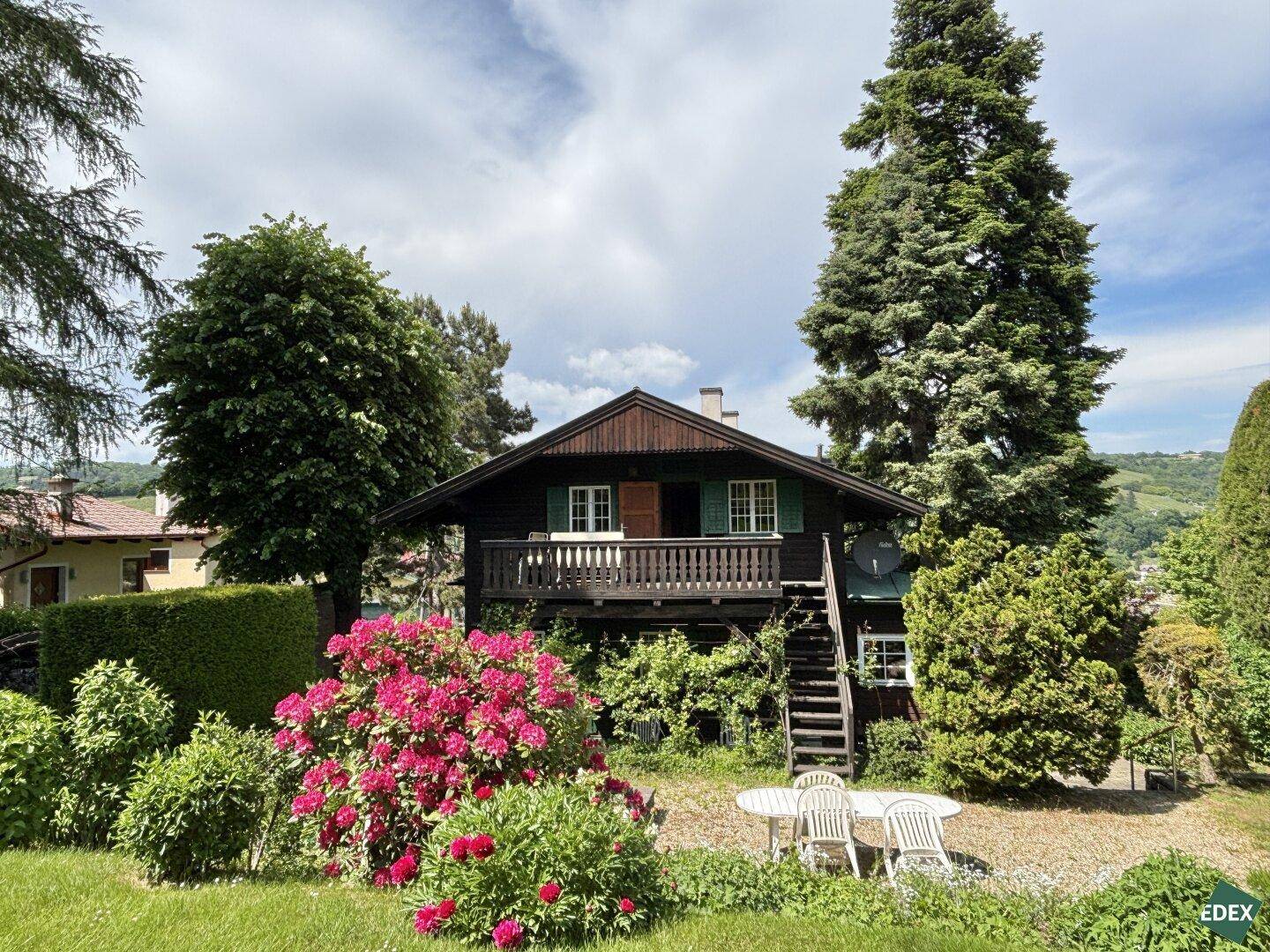 Charmantes Holzhaus mit blühendem Vorgarten und weißer Gartensitzgruppe.