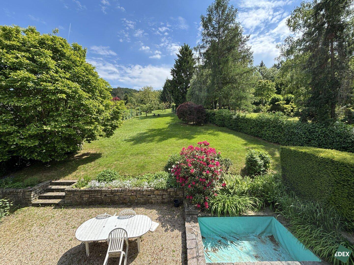 Gartenbereich mit leerem Pool, weißem Gartentisch und weitem Rasen.