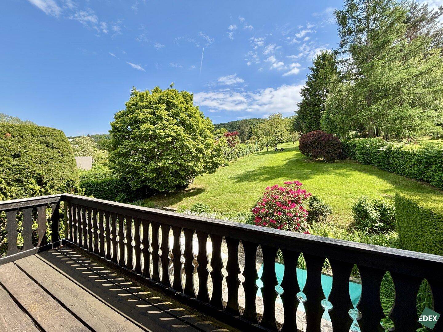Holzbalkon mit geschnitztem Geländer und Blick auf den blühenden Garten.