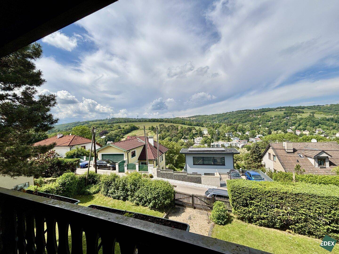 Blick von einem Balkon auf die Wohnsiedlung und die bewaldete Hügellandschaft.