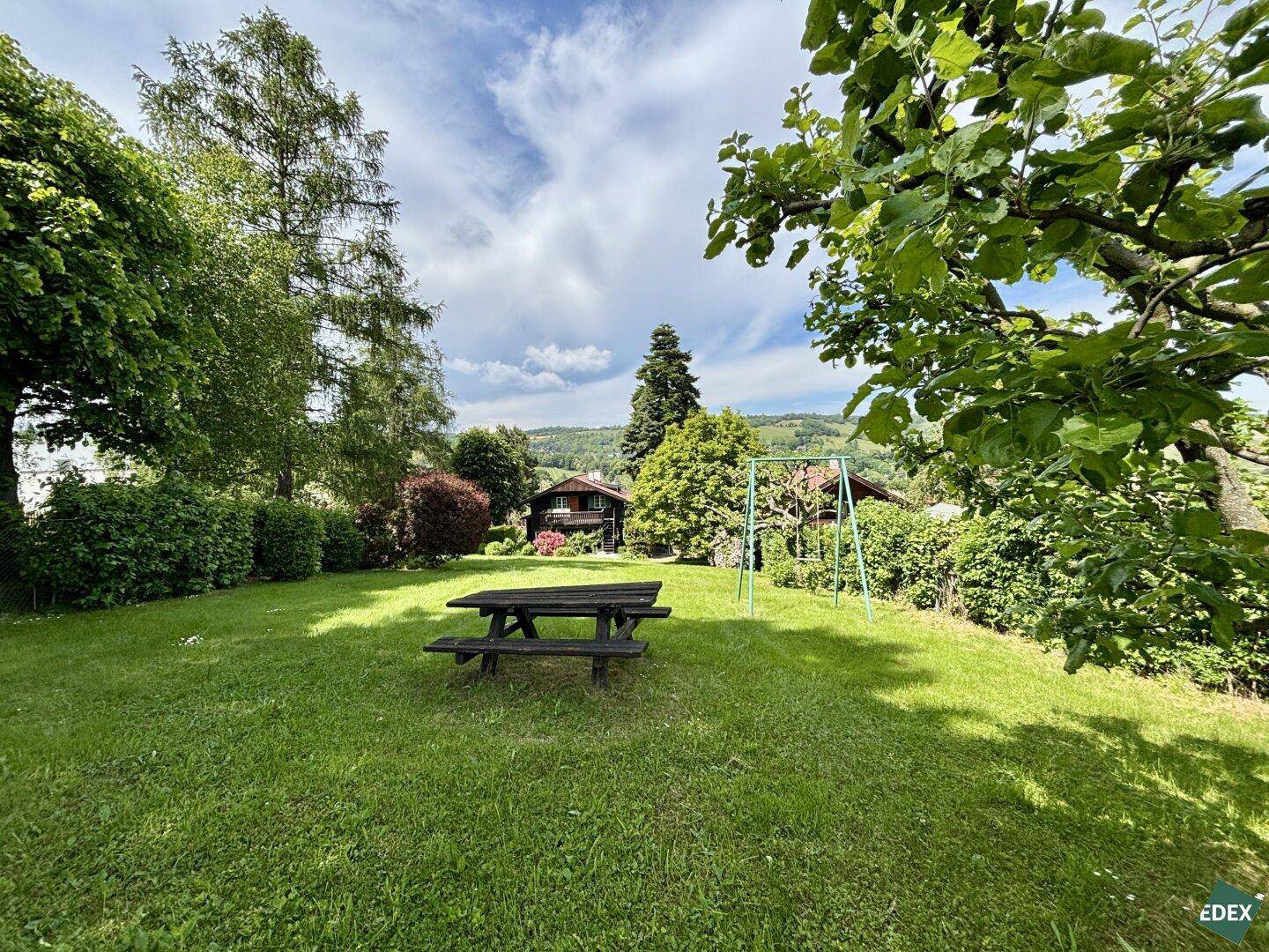 Sonniger Garten mit Rasenfläche, Picknicktisch und Schaukel für Kinder.