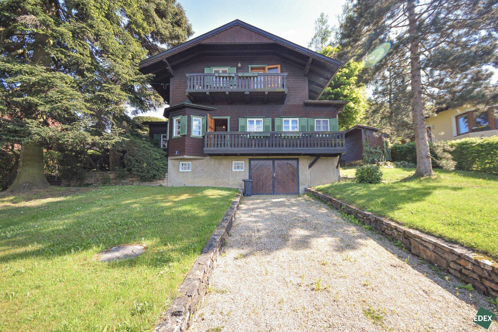 Frontansicht eines Holzhauses im Chalet-Stil mit Balkonen und Kiesauffahrt.