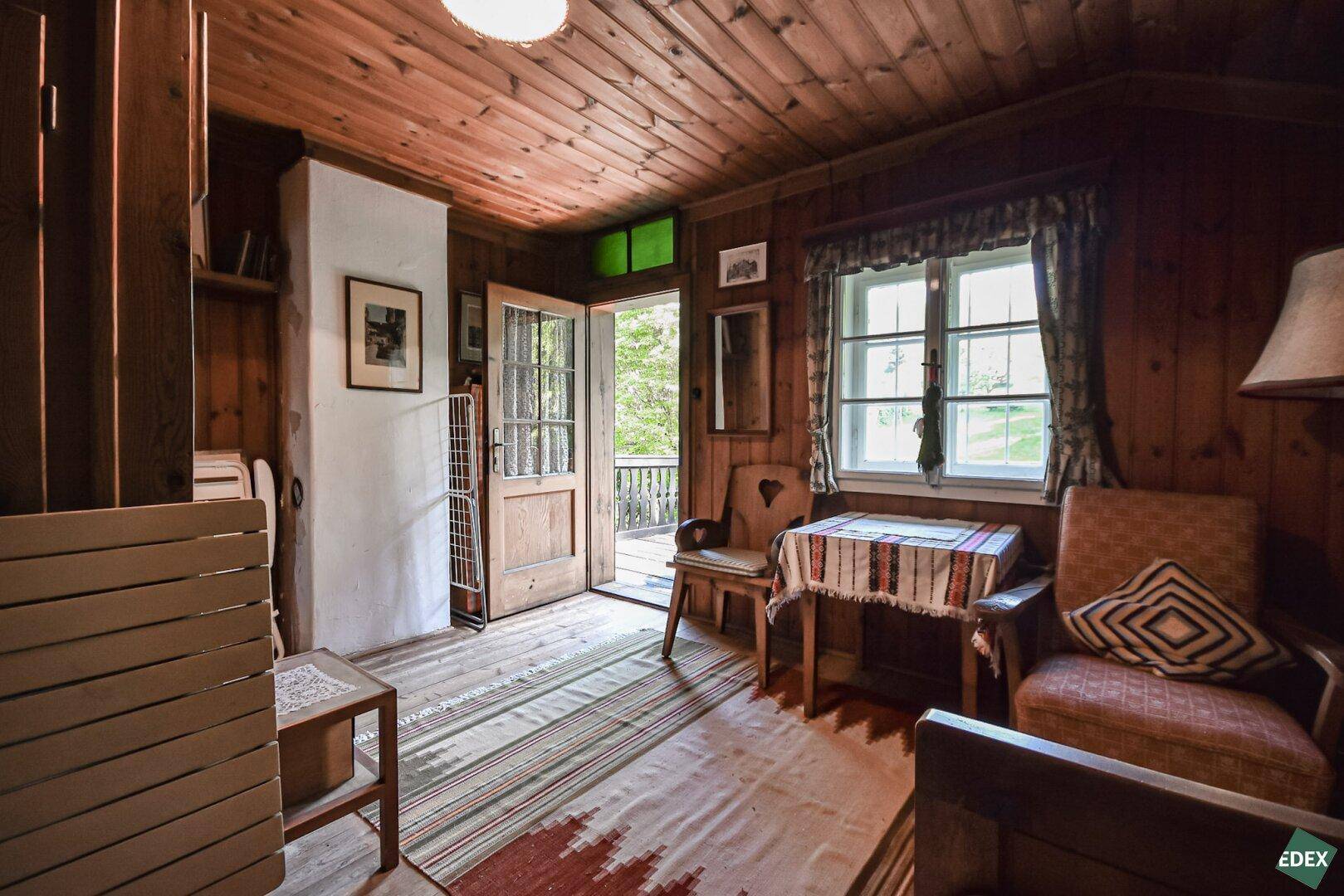 Rustikales Wohnzimmer mit Holzboden und -wänden, traditionellen Möbeln und Zugang zum Balkon.