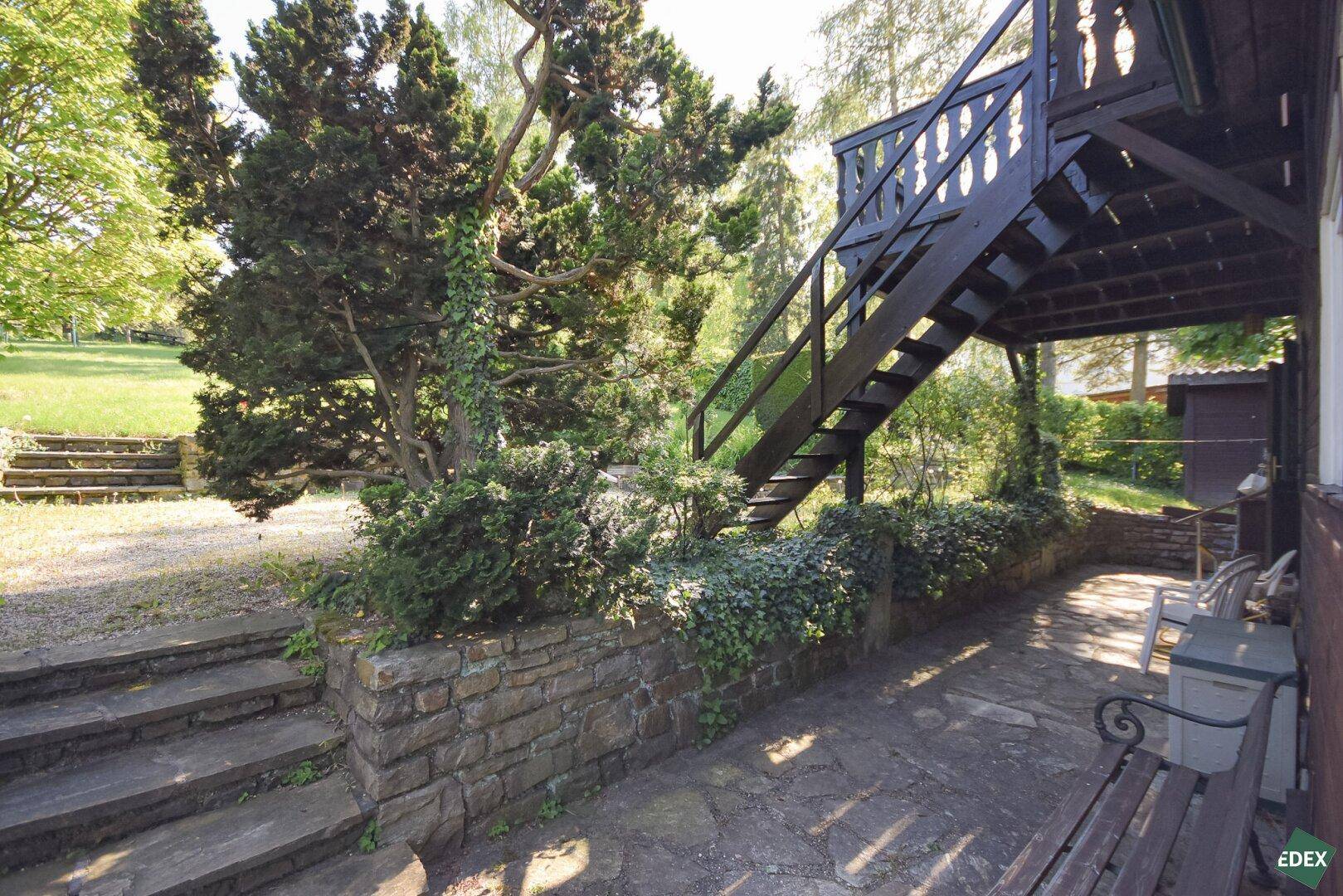 Steintreppe und gepflasterter Bereich im Garten, der zum Haus und den oberen Ebenen führt.